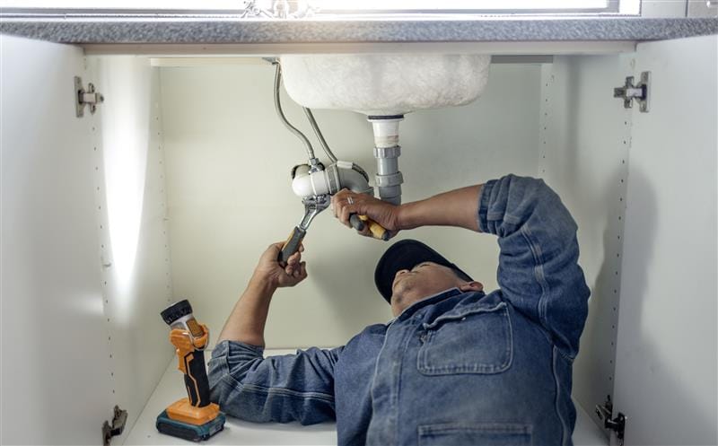 Plumber repairing pipes beneath a bathroom sink in Moreno Valley